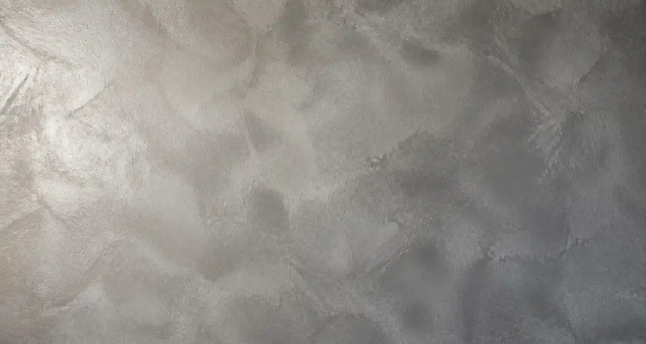 Détail macro d'un béton ciré taloché : nuages gris minéral et finition satinée en lumière rasante